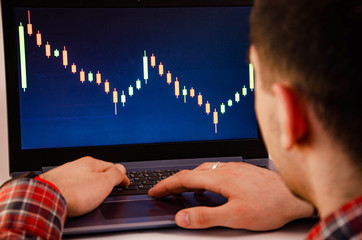 Trading on the exchange. Men's hands in a plaid shirt at a laptop. On-screen rates, promotions....