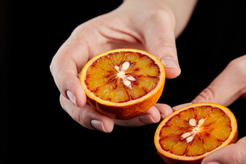 Blood or red orange fruit halves in hands on black background