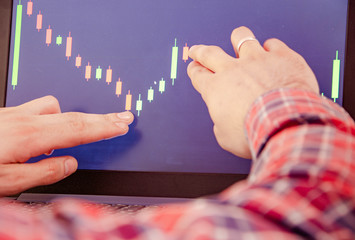 Trading on the exchange Men's hands in a plaid shirt behind a laptop show on the graph. On-screen...