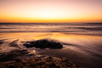 Fototapeta na wymiar Swirl pattern of a waves rolling onto beach at sunset time