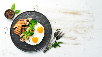 Healthy breakfast. Fried egg with broccoli, mushrooms and bread. On a black stone plate. Top view.