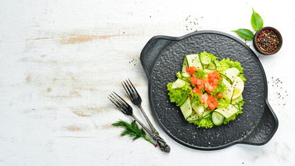 Salad with cucumber, salmon and lettuce. Healthy food. On a black stone plate. Top view.