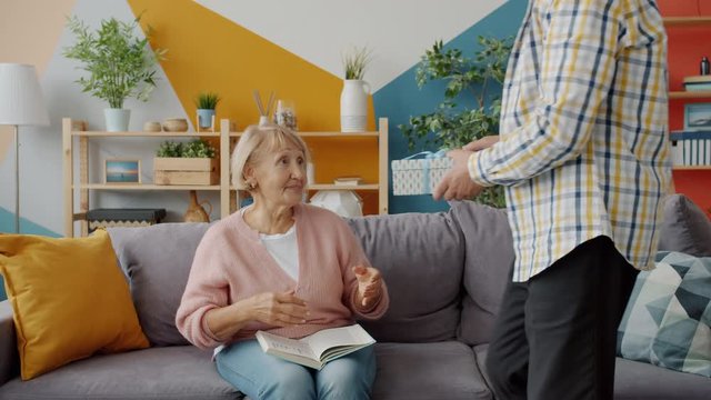 Loving husband elderly man bringing gift box to happy wife making surprise on holiday, woman is higging and kissing caring spouse. Presents and family concept.