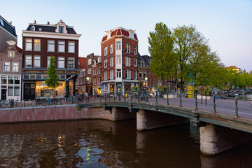 Naklejka premium Budynki i łodzie wzdłuż kanału w czasie zachodu słońca w Amsterdamie, Holandia