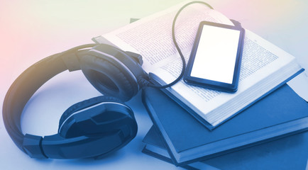Audio book concept with headphones, tablet, open book and pile of books. Listening to book. Modern education. Trendy blue color image. Copyspace.