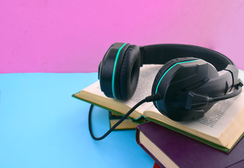 Audio book concept. Close up headphones, open book and pile of books on colored background. Listening to book. Modern education. Copyspace.