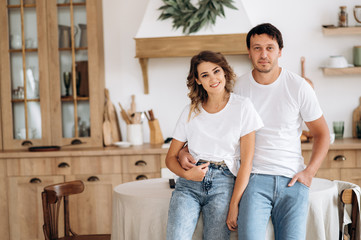 Morning at home. Portrait of a beautiful couple in love in the kitchen. The guy and the girl are stylishly dressed in white t-shirts and jeans