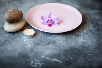 Obraz na płótnie Canvas Orchid flower floating in a saucer filled with water, balancing massage stones and a burning candle