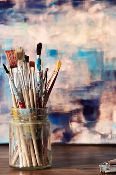 Paint brushes and abstract artwork on canvas