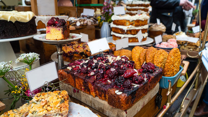 Market stall table covered with various cakes, bake bars, biscuits, and other treats