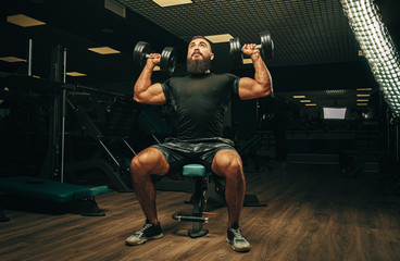 Fototapeta na wymiar Muscular young man lifting weights in a dark gym