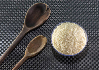 Grains of cereal rice on a dark background in a jar next to wooden spoon