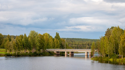 Fototapeta na wymiar Bridge over the pond. A fabulous landscape of a Finnish lake in the midst of a dense Scandinavian green forest. The concept of calm and quiet rest in the most environmentally friendly country.