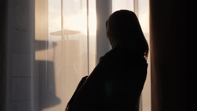 A woman with a warm plaid on the ples looks out the window