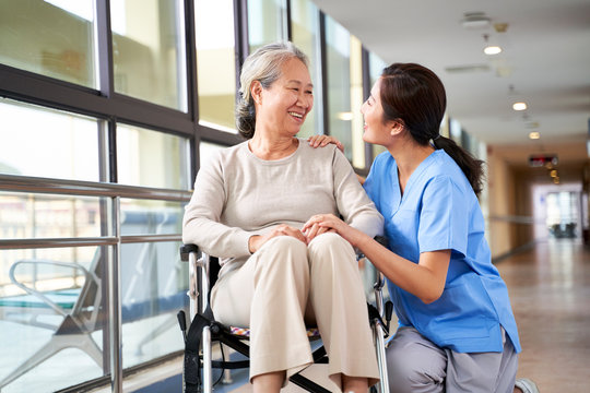 friendly asian caregiver talking to senior resident in nursing home