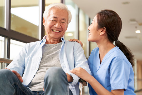 young friendly asian female caregiver talking to elderly man in nursing home