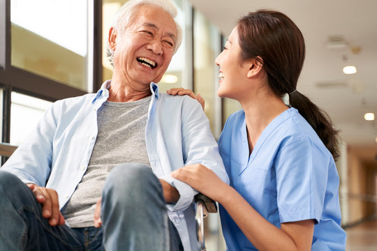 young friendly asian female caregiver talking to elderly man in nursing home