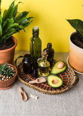 Set of eco friendly kitchen items. wooden cutlery, glassware, a flower in a ceramic pot, natural oils and a sliced ​​avocado on a linen tablecloth against a yellow wall. Zero waste and plastic free