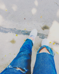 Fototapeta premium Woman's legs with blue fashion jeans and white sneakers on street for travel concept