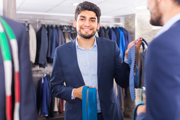 Smiling male is picking up tie for jacket in front of the mirror