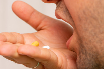 Man taking two pills yellow and white as a medicine