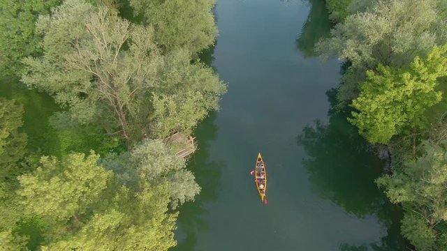 DRONE, TOP DOWN: Carefree tourists paddle their canoe along the tranquil river Krka on a sunny summer day. Cinematic shot of a group of friends going on a canoeing adventure in Slovenian countryside.