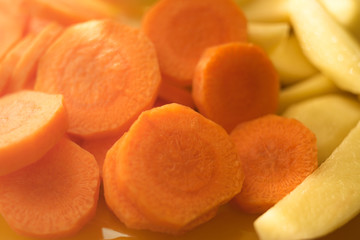Raw round slices of carrots and potatoes close-up.