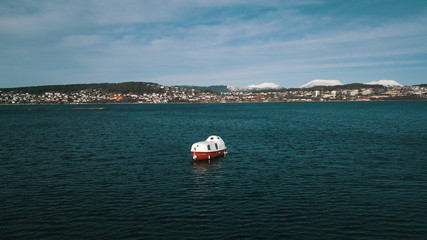 A lifeboat, moored alongside the bay. In the background a city against the backdrop of snowy mountains in Norway.