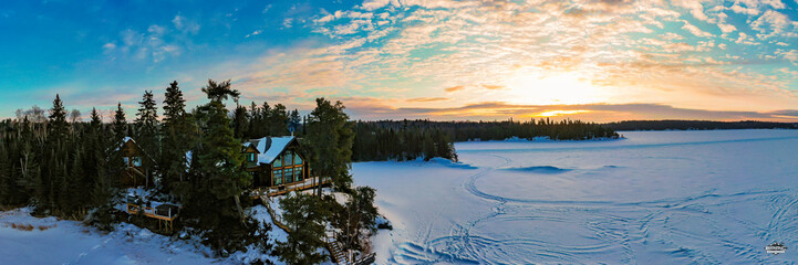 A snowy winter cabin overlooking a frozen lake during a beautiful bright sunrise.