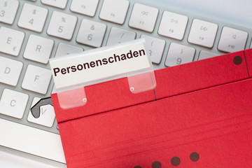 Roter Hängehefter mit Reiter und dem Text: Personenschaden. Der Ordner liegt auf einem Computer...