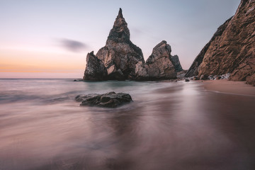 Rocky sea stacks at Portugal Ursa Beach at Atlantic Ocean coast in sunset light. Foamy waves rolling on picturesque landscape vacation scene