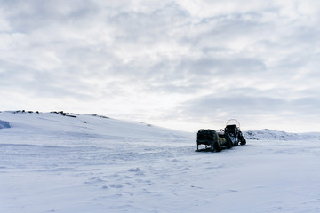 an empty snowmobile with trailed sled stands in the middle of the tundra covered with pure white...