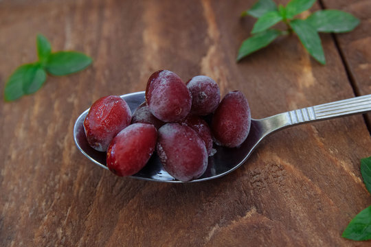 Frozen red dogwood berries lie on a tablespoon on a brown wooden background with green mint leaves