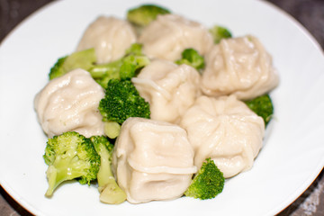 Meat dumplings on a white plate with broccoli