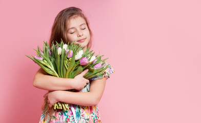 Cute smiling child girl holding bouquet of spring flowers tulips isolated on pink background....
