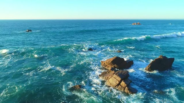 Waves surge consecutively against the reefs on the broad blue sea in western Portugal.