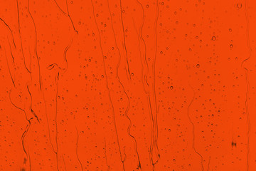 Raindrops on an orange background. Drops of water flow down the surface. The intensity of the red color Lush Lava.