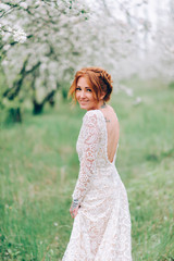 Fototapeta na wymiar Young beautiful woman in a white dress is standing in a blooming garden.