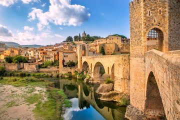 Besalu, Girona, Catalonia, Spain. Famous landmark. Old medieval Romanesque bridge Besalu over the river Fluvia on a sunny summer day. - obrazy, fototapety, plakaty