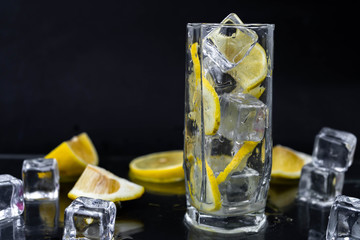 Sparkling water with lemon and ice, white soda in glass on black background, refreshing cold drink