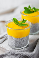 Healthy and delicious homemade vegan breakfast, simple and light meal - chia pudding prepared with coconut or rice milk with ripe mango puree on top. Fresh green mint. Wooden background,