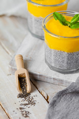 Healthy and delicious homemade vegan breakfast, simple and light meal - chia pudding prepared with coconut or rice milk with ripe mango puree on top. Fresh green mint. Wooden backgroun