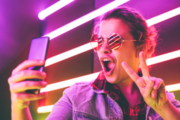 Portrait of modern young woman in glasses making selfie at the neon light.