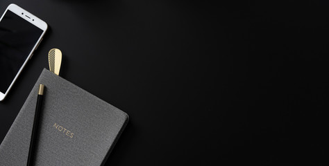Writing with pencil, notebook and phone with blank screen on balck office desk with copy space . Business and technology on a table on black background. Panoramic banner.