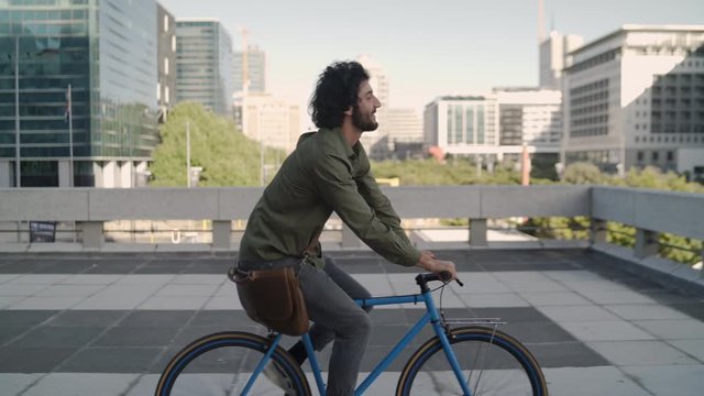 Cheerful professional young man with his brow bag going to work on bicycle in city street - Powered by Adobe