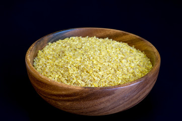 Dry bulgur close-up in a wooden bowl on a dark background. Concept of Oriental cuisine dishes