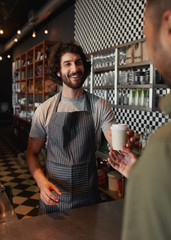 Smiling mature waiter giving take away coffee to man at cafeteria