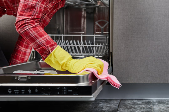 The woman hands in yellow gloves cleaning dishwasher panel with pink rag in kitchen.close up.