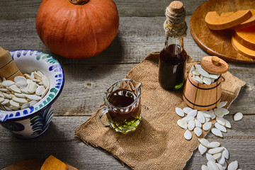 Cold pressed Pumpkin seed oil in a glass bottle and gravy boat, raw pampkin decorated with seeds in pounder