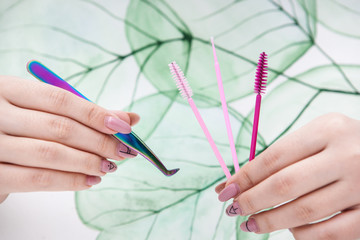 tools for eyelash extensions in hands on a background with a natural pattern